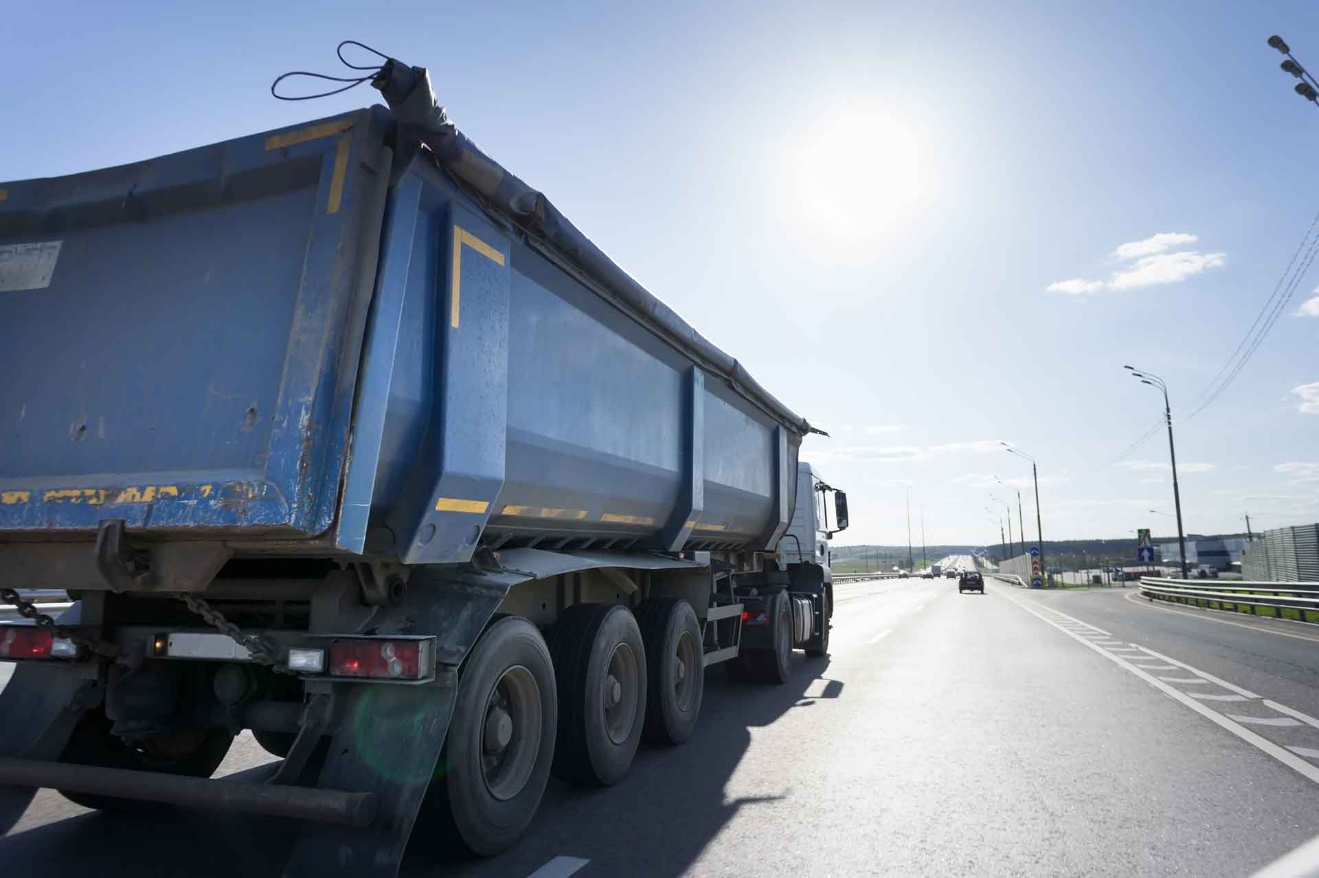 Dumpster truck driving down road on a sunny day
